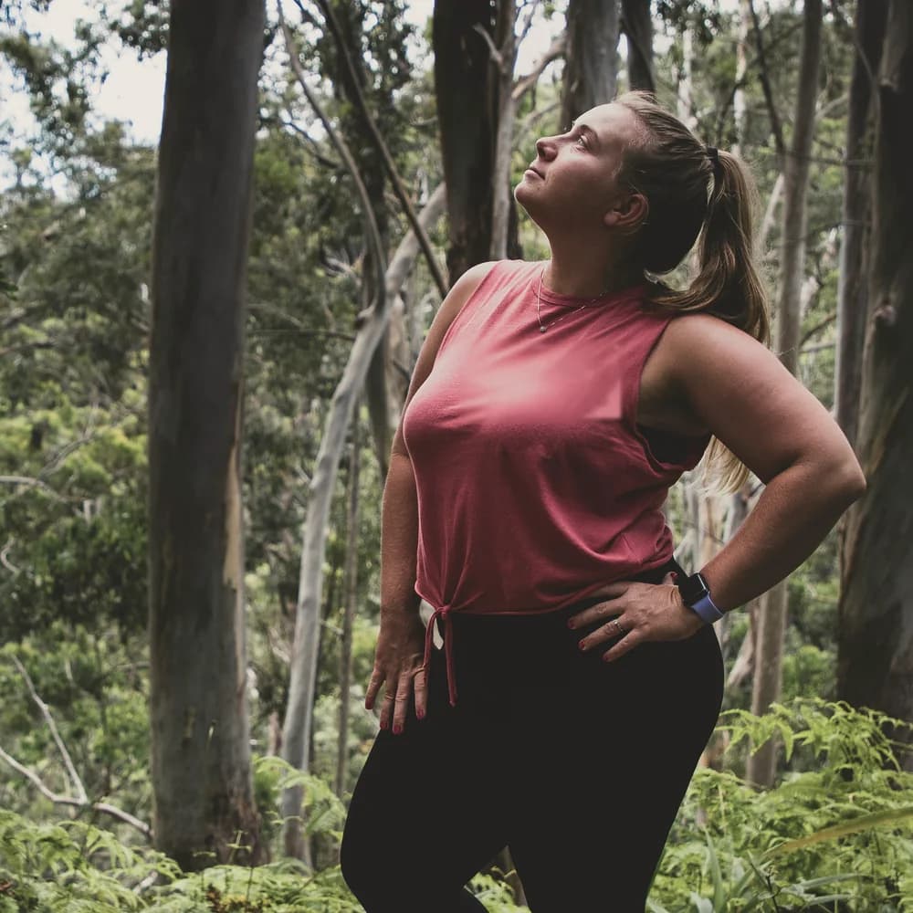 A woman pausing on a woodland trail, looking up through the trees