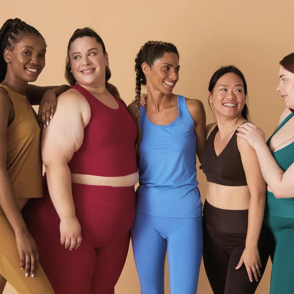 Several women of different body types and backgrounds standing together and smiling