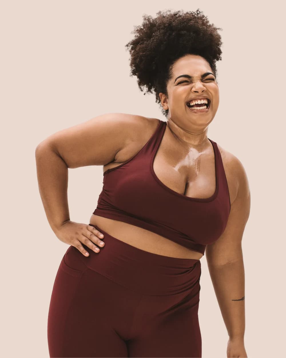A woman laughing in athletic wear against a warm terracotta backdrop