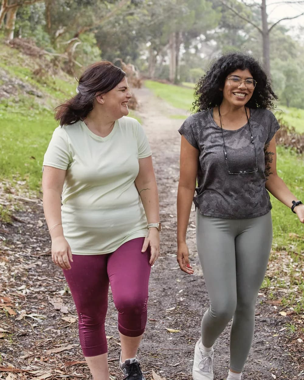 Two women walking and laughing together on a tree-lined trail